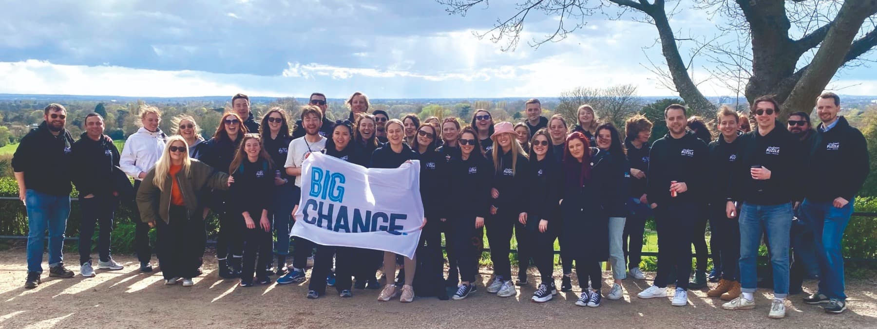 The Professor Puzzle team gathered outdoors holding a Big Change banner